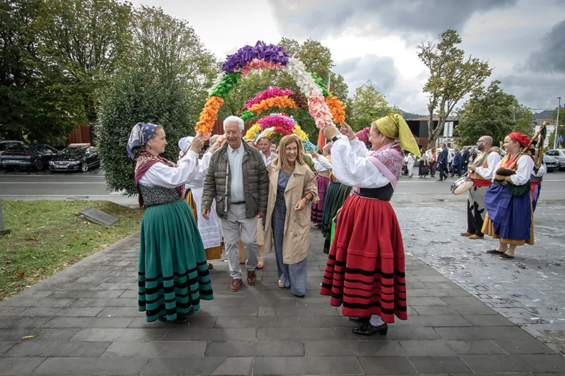 La presidenta y el alcalde de Meruelo atraviesan el arco floral formado por la Agrupación de Danzas Virgen de las Nieves de Torrelavega (FOTO: José Cavia)